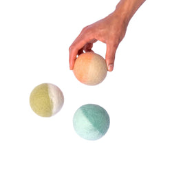 Three wool dog toys in multiple colors and person holding one